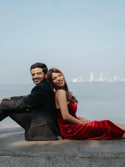 A relaxed and happy pose, sitting back-to-back against the sea wall, showcasing the couple's comfortable and playful relationship.