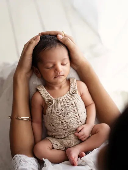 A mother's hands gently cradling her sleeping newborn's head. A beautiful detail shot that shows the tenderness and care of a new mom.