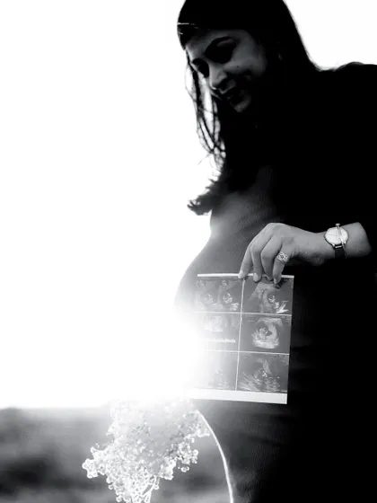 A high-contrast black and white shot where the sun flares behind the mom-to-be, creating a halo effect as she looks at her sonogram.