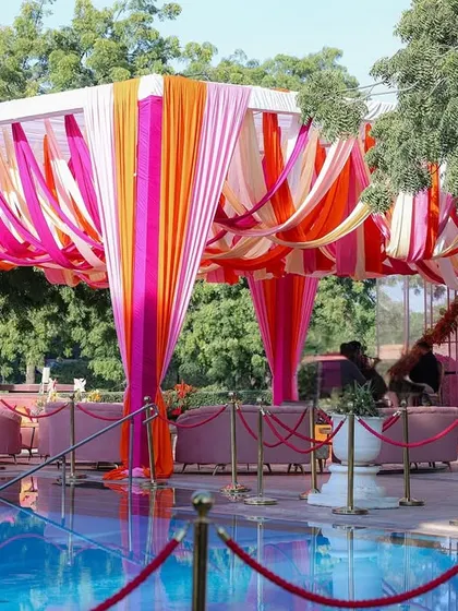 A vibrant poolside seating area with lounges set under a canopy of pink and orange hanging drapes, perfect for a high-tea event.