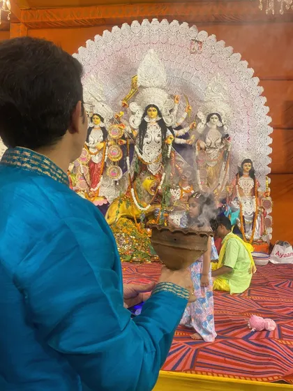 A man in traditional blue kurta offers prayers with the dhunuchi during Durga Puja. The focus is on the act of devotion and the vibrant colors of the festival.