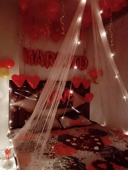 Another view of the romantic room setup, showing the "MARRIED" foil balloons and heart-shaped balloons above the bed. The combination of the sheer canopy and warm lights creates a dreamy and celebratory feel.