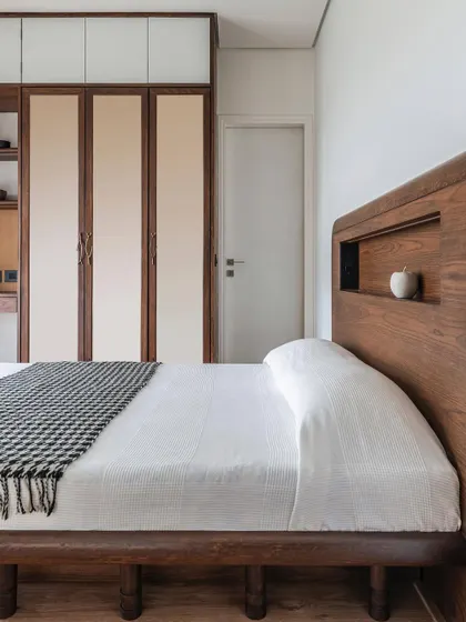 A bedroom in Apartment 1501, a compact city getaway for a young couple. The custom bed with a built-in headboard niche maximizes space, while the warm wood and simple color scheme create a cozy and inviting feel.