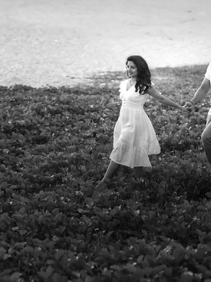 A candid black and white photo of a couple walking along the water's edge. The monochrome style gives this simple, happy moment a classic, storybook quality.
