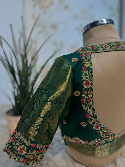 A deep green blouse with a contrasting red floral embroidery along the back and sleeve borders, paired with a traditional zari sleeve.
