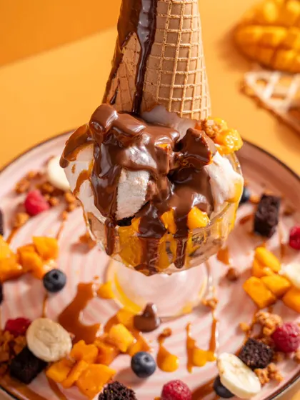 An over-the-top mango sundae from Bastian. This shot captures the playful and indulgent nature of the dessert, with its ice cream cone and multiple toppings.