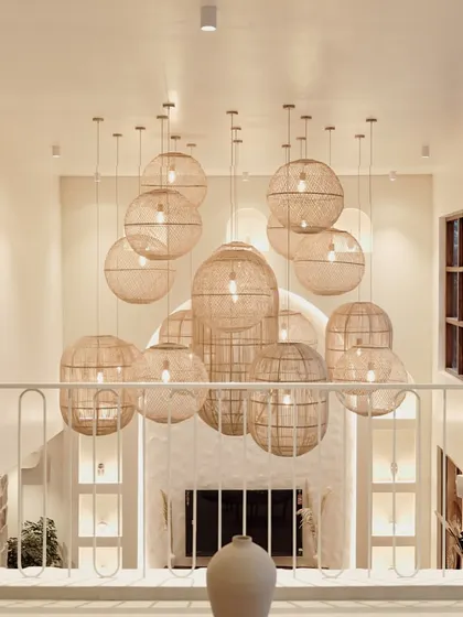 Looking down from the mezzanine, you can see the dramatic cluster of woven pendant lights that serve as a sculptural centerpiece. This feature draws the eye upwards, accentuating the vertical space and adding a layer of artisanal texture.
