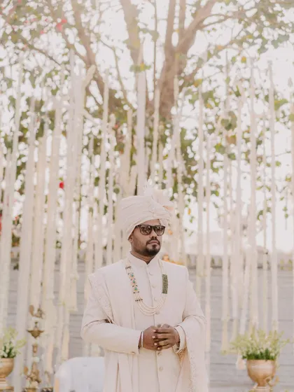 The groom waiting patiently at the mandap. The soft, natural light and beautiful decor create a serene and classic portrait.