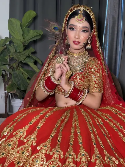 A full-length seated portrait of a bride in her red lehenga. The peacock feather adds a touch of traditional elegance to the shot.