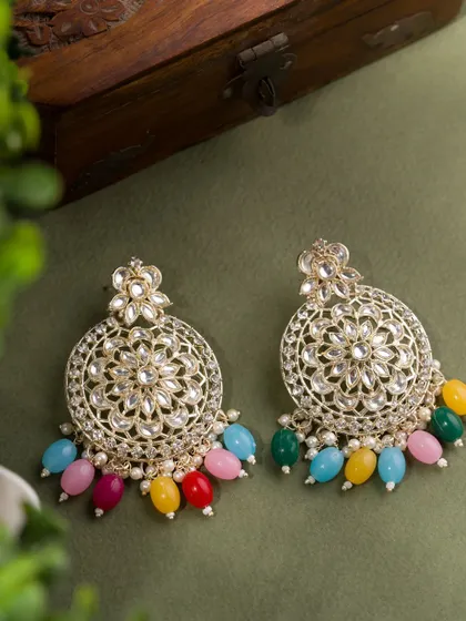 A pair of traditional Kundan-style earrings with colorful beads. The natural, leafy background provides a beautiful contrast to the intricate jewellery.