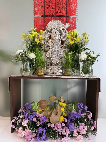 A sacred altar featuring a silver idol of Lord Shrinathji, flanked by fresh lilies and bamboo shoots, with a beautiful arrangement of colorful flowers at its base.