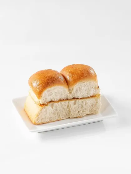 Soft, buttery pav buns presented on a clean white plate. This simple, high-key photograph highlights the freshness and fluffiness of the bread, a key component of the classic Pav Bhaji.