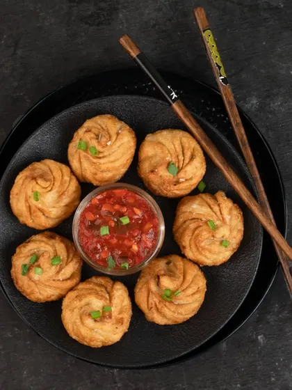 Another angle of these delicious fried momos. The composition and dark background emphasize the texture and shape of the dumplings, making them the hero of the shot.