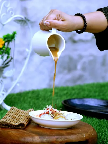 A server pours a rich, aromatic broth over a bowl of noodles, an action shot that highlights the fresh and interactive elements of our dining experience.