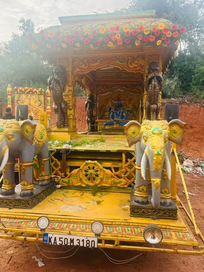 A procession chariot with a deity seated inside, flanked by two decorative elephants and adorned with flowers.
