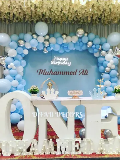A simple and classic decor for Muhammed Ali's first birthday. The blue and silver balloon arch frames a "ONE" table and light-up name sign, creating a timeless and celebratory setup.