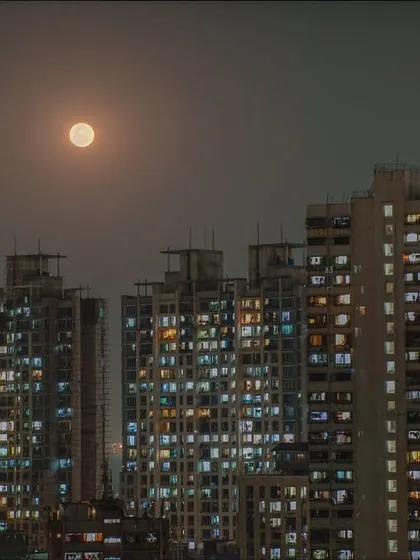 A full moon glows through the haze above a dense cluster of residential buildings in Mumbai at night.