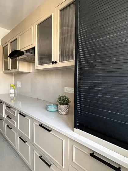 A newly installed kitchen in Nirala Estate, featuring off-white paneled cabinets, sleek black handles, and fluted glass upper cabinets for a touch of elegance.