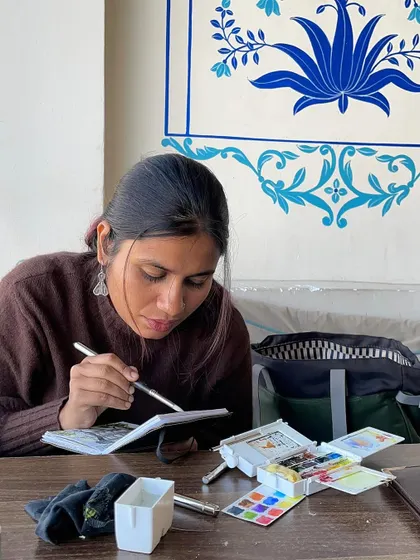 A close-up of me painting at a cafe in Udaipur, with a beautiful mural in the background. The city is full of artistic inspiration.