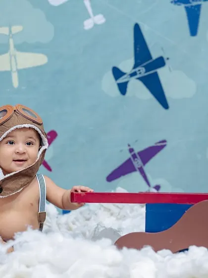 This sitter session features a little pilot in an aviator hat, sitting among fluffy clouds with a toy plane, against a backdrop of vintage aircraft.