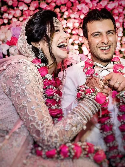 A candid moment of pure laughter between a bride and groom during their Muslim Nikah ceremony. The image is filled with joy and highlights the beautiful floral decor.