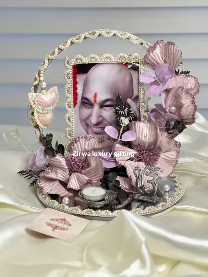 A delicate and shimmering Guruji Darbar with metallic pink and purple flowers on a mirrored base. The design includes a pearl-studded frame and a hanging heart charm, adding a touch of elegance.