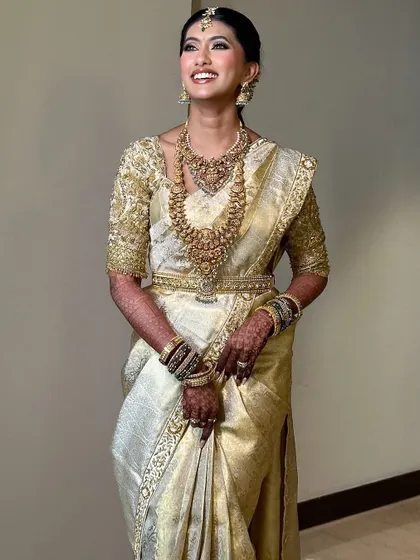 This bride looks radiant and happy in her classic off-white and gold wedding attire. The custom blouse and traditional jewelry complete her timeless look.