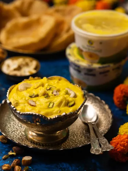 A festive shot of Shrikhand Puri for Gudi Padwa. The vibrant yellow of the shrikhand against the deep blue background creates a visually stunning contrast.