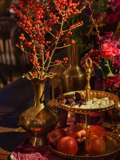 A detail shot of the decor, featuring a brass vase with red berries, a tiered tray with dates, and fresh fruits. These elements evoke the colors and flavors of a Moroccan market.