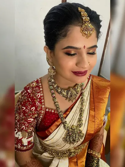 A close up of a traditional South Indian bridal makeup look. The focus is on the golden shimmery eyeshadow, perfectly winged eyeliner, and a deep red lip, set against flawless skin. This look is designed to last through all the wedding day ceremonies.