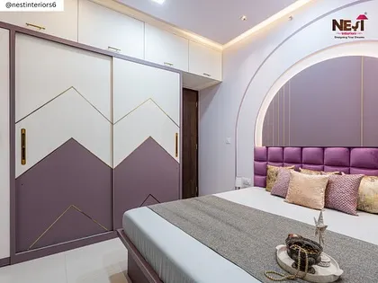This bedroom design uses a bold purple tufted headboard set within an arched niche. The chevron-patterned sliding wardrobe adds a modern geometric element to the room.