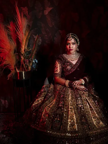 A regal, seated portrait of the bride in her heavily embroidered lehenga. The dark, moody background with a pop of red makes her stand out as the center of attention.