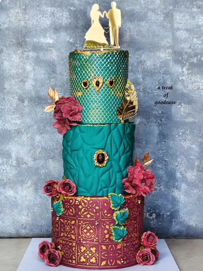 For this grand wedding celebration, I designed a three-tiered cake with rich jewel tones. Each tier features a different non-fondant texture, from a quilted pattern to geometric embossing and a gold-stenciled base, all brought together with deep red sugar flowers.