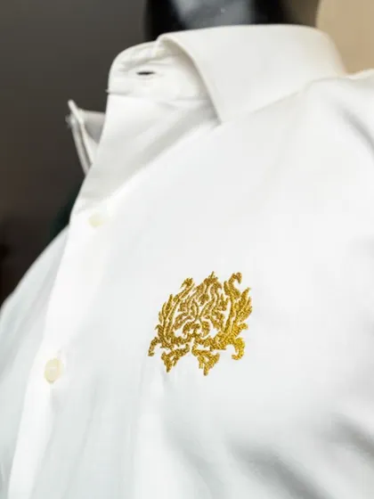 We can add custom embroidery to our shirts, like this intricate gold logo. This level of personalization is perfect for corporate branding or adding a unique monogram to a gift.