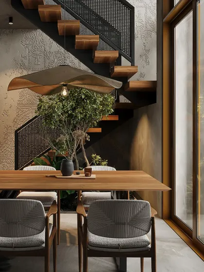A dining space from a Bangalore project, featuring a solid wood table and woven chairs. The room is situated next to a floating staircase with an indoor planter underneath.