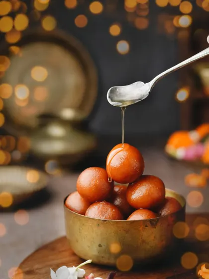 Baby gulab jamuns getting a final drizzle of syrup, framed by beautiful bokeh lights. This shot feels festive and magical, making a classic sweet feel extra special.