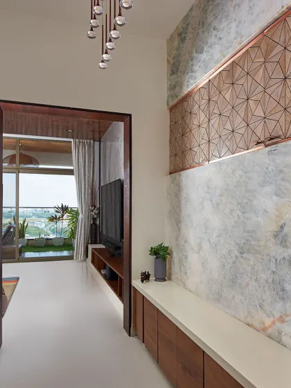 In the Sobha Indraprastha apartment, the foyer features a wall clad in onyx marble with a CNC-cut wooden panel. This decorative panel is strategically designed to hide the electrical board while adding to the aesthetic.