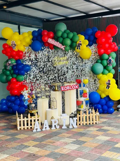 A vibrant Roblox-themed birthday party, perfect for gamers. This outdoor setup features a silver shimmer wall backdrop framed by a colorful balloon garland in the game's signature red, blue, yellow, and green, along with character cutouts.