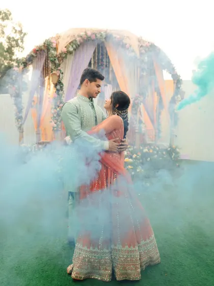 A romantic portrait of the couple surrounded by blue smoke bombs during their Haldi event. It adds a touch of modern drama to the traditional ceremony.