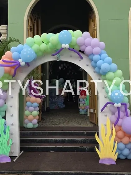 An elaborate entrance designed to look like an underwater castle, with balloon arches, seaweed props, and a personalized welcome sign.