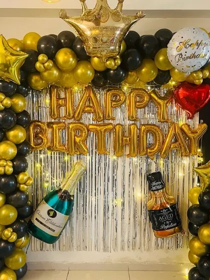 A fun and festive birthday backdrop for an adult, featuring black and gold balloons, a crown, and bottle-shaped foil balloons.