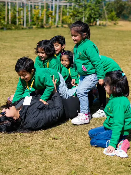 A joyful moment as a group of students playfully pile on top of their teacher on the grass.