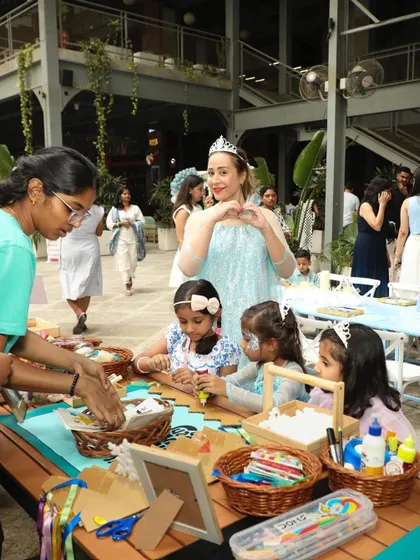 The mother of the birthday girl makes a heart sign as she watches the children enjoying the craft table at the Mystic Wonderland party.