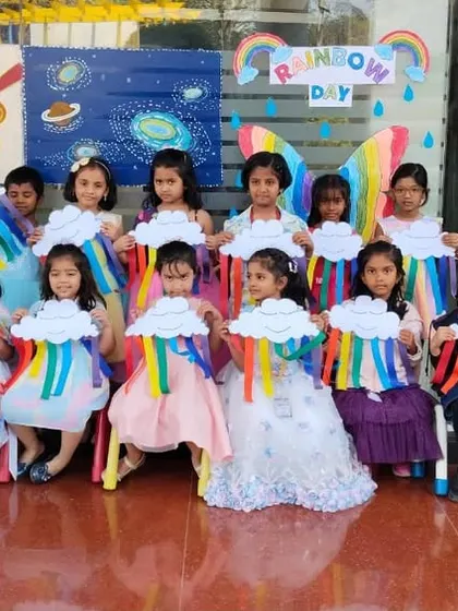 A group of girls in beautiful dresses hold up their rainbow crafts, showcasing their artistic work.