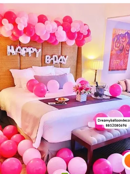 A pink-themed birthday surprise in a hotel room. The decoration includes 'HAPPY B-DAY' foil balloons over the bed, with pink balloons scattered on the floor and bed for a fun, celebratory feel.
