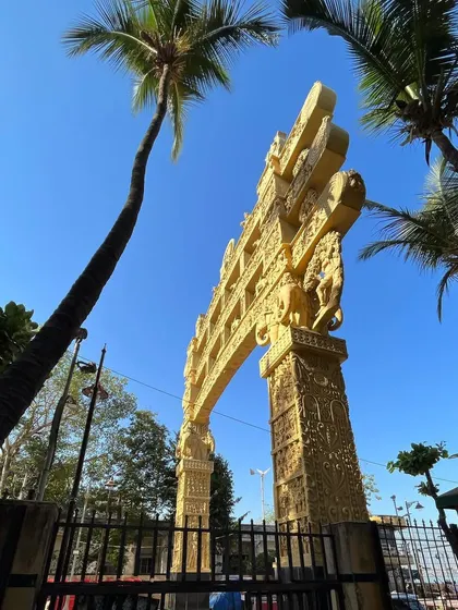 An upward-looking shot of the ornate golden gate at Chaitya Bhoomi, framed by palm trees.