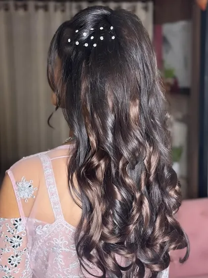 A detailed shot of a beautiful sangeet hairstyle. Soft curls are gathered into a half-up style, adorned with delicate pearl pins for a touch of elegance.