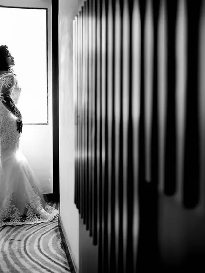 A dramatic bridal silhouette shot against a bright window. This black and white image uses strong contrast and composition to create a powerful and elegant portrait, capturing a quiet moment of reflection for the bride on her wedding day.