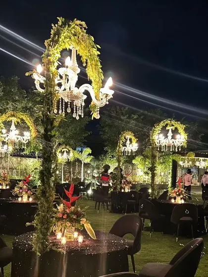 A dreamy sit-down dinner setup on a lush lawn. Each table features a sparkling tablecloth and a centerpiece with a chandelier wrapped in greenery, creating a magical ambiance.