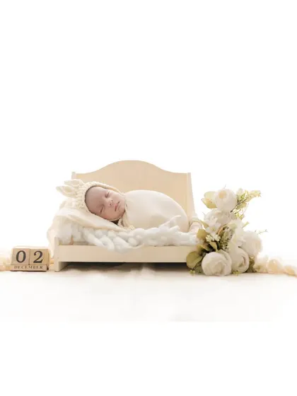 A sleeping newborn lies on a miniature bed, with wooden blocks indicating the date. This is a beautiful way to commemorate the baby's birth date while creating a delicate and artistic portrait.